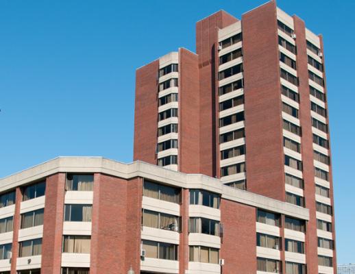 Brick building with a low rise on the left and a high rise on the right, blue skies in the background.